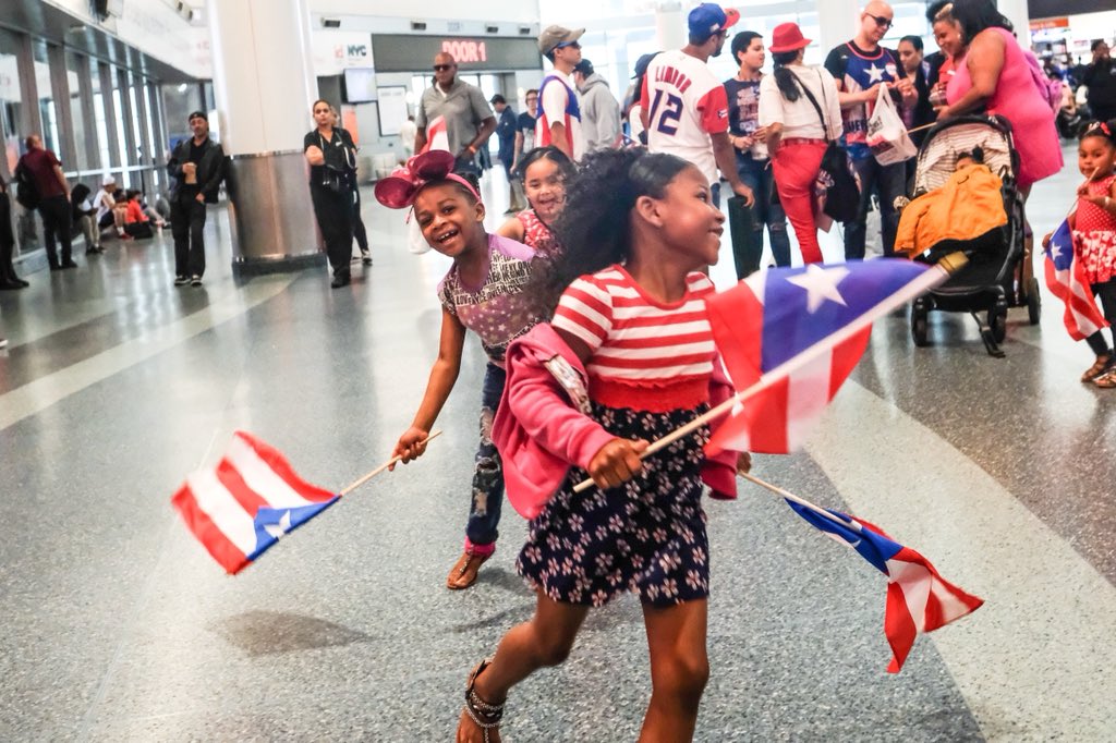 Three Children laugh at the ferry terminal waving flags of Puerto Rico.