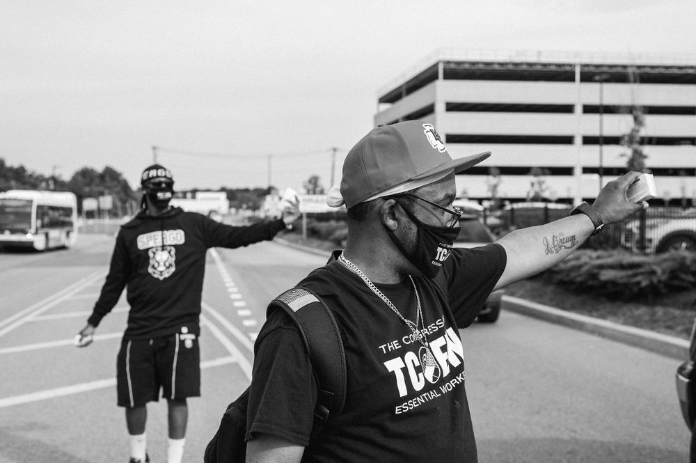  Black and white photograph showing two men distributing union authorization cards on a road in front of large buildings.