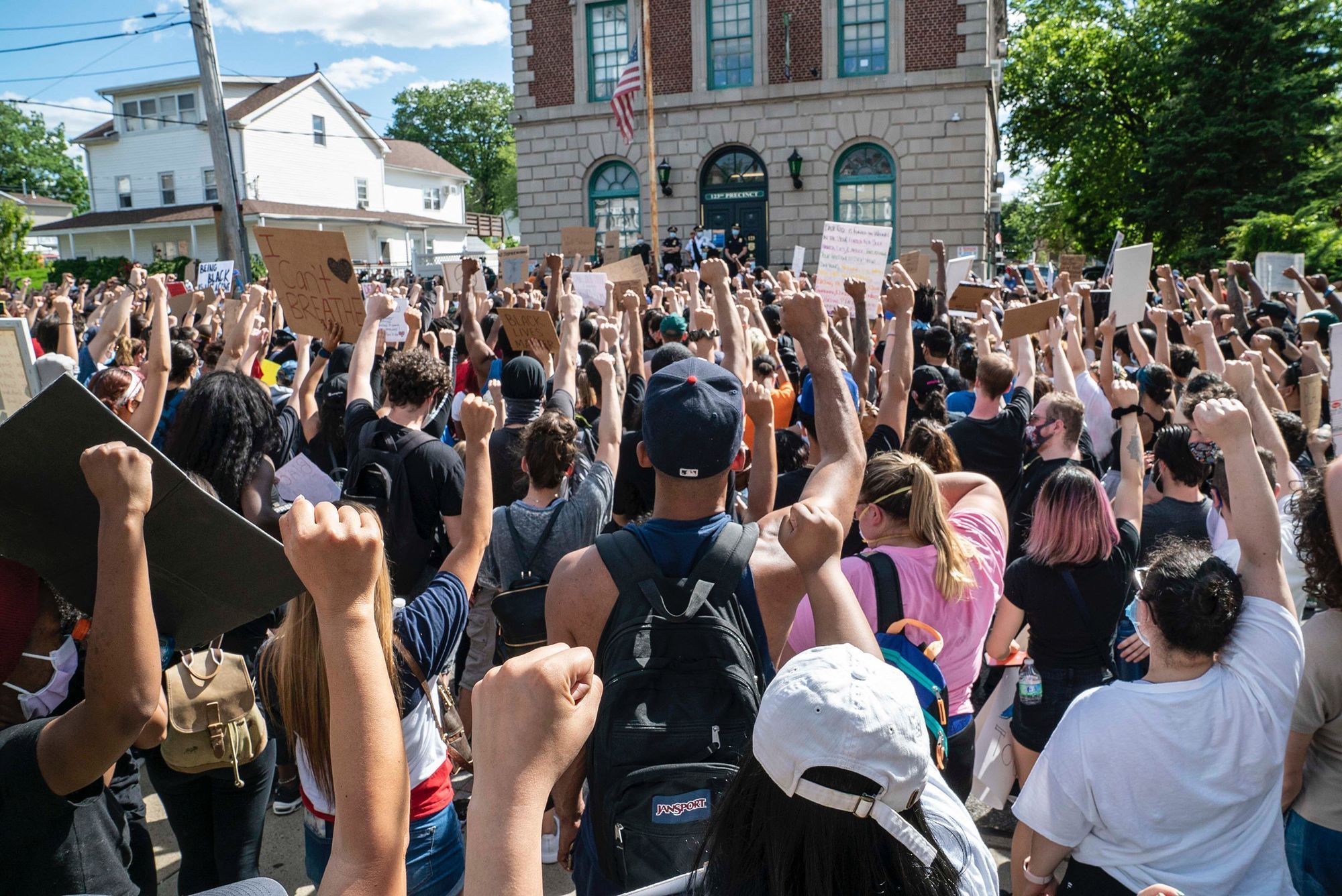 A very large crowd of people raise their fists in solidarity in front of a police station during a demonstration . Many of the demonstrators hold uo signs.