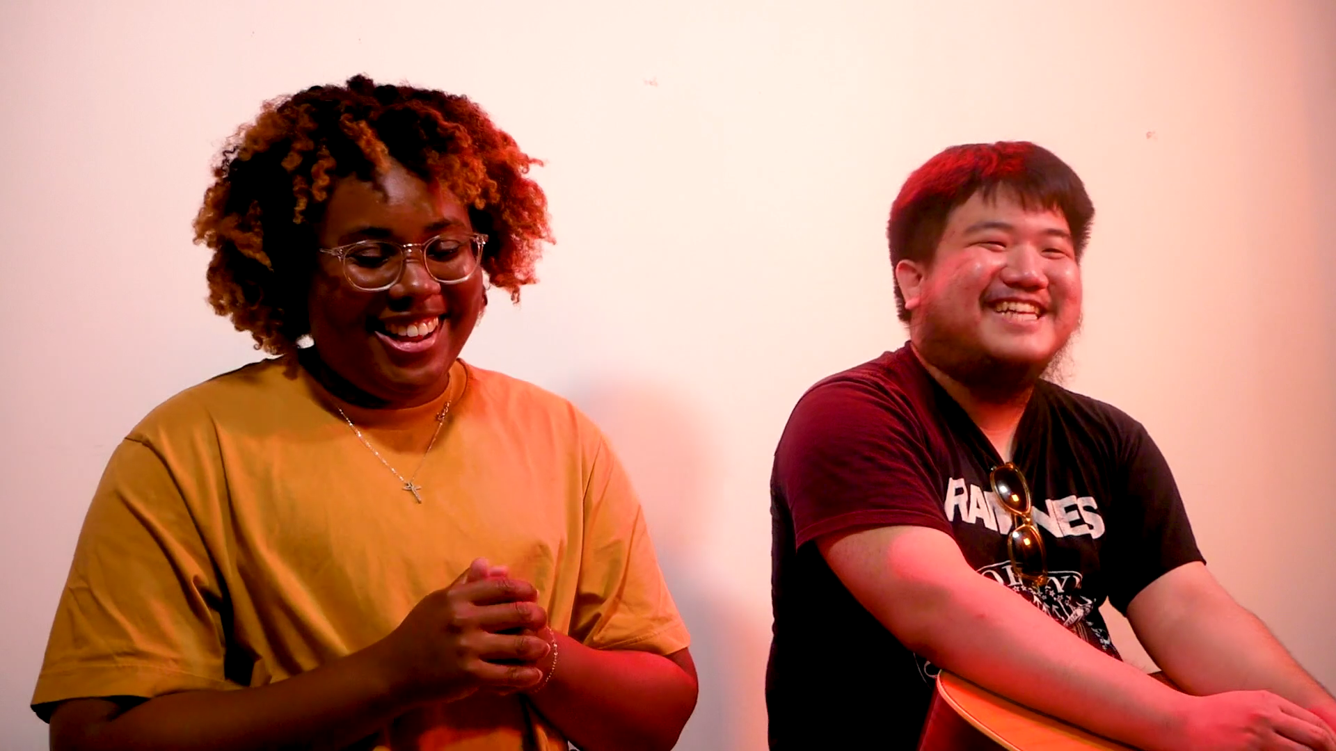 A female on the left wearing a mustard yellow shirt and a male on the right weaing a black Ramones band t-short, both with large smiles.